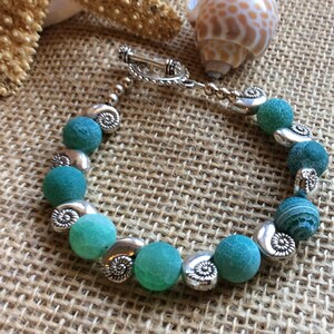 May include: A green agate bead bracelet with silver shell-shaped accents and a toggle clasp.