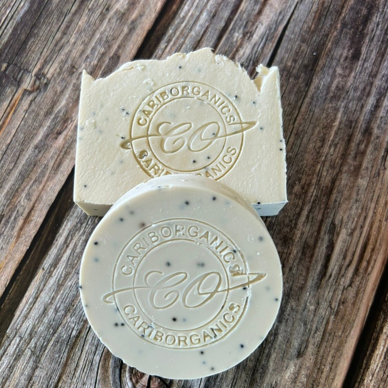 K&ouml;nnte beinhalten: Zwei runde Seifenst&uuml;cke mit wei&szlig;er Basis und schwarzen Flecken. Die Seife tr&auml;gt den Text "Cariborganics CO" in einem Kreis auf der Oberseite.