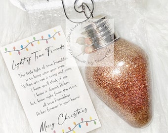May include: A gold glitter Christmas ornament shaped like a light bulb with a tag that reads "Light of True Friends" and a poem about friendship. The tag also has a string of colorful lights.