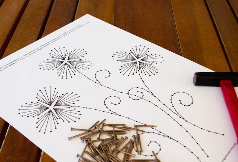 May include: A white paper with a black floral design, nails, and a hammer. The floral design features three starburst-like flowers connected by stems with small dots. A black hammer with a red handle is on the right.