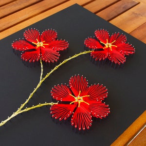 May include: Red string art flowers with yellow centers on a black background. The flowers are connected by a yellow stem.