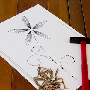 May include: A black and white line drawing of a flower with a stem and two curls on a white sheet of paper. A hammer with a red handle and a pile of nails are on the paper.