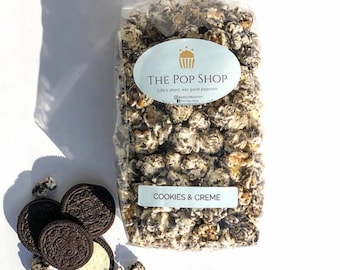 May include: A bag of Cookies & Creme popcorn with a white label that says "THE POP SHOP" and "Life's short, eat good popcorn". There are also some Oreo cookies scattered around the bag.