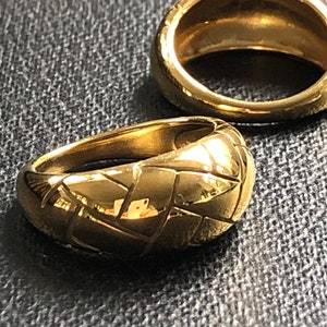 May include: Two gold-toned rings. One ring has a simple, smooth band. The other ring has a textured, woven design.
