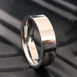 May include: A silver-toned ring with a flat, polished surface. The ring is thick and has a simple design.