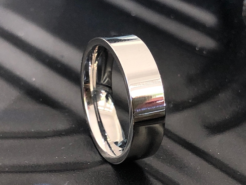 May include: A silver-toned ring with a flat, polished surface. The ring is thick and has a simple design.