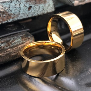 May include: Two gold-colored metal rings, one slightly larger than the other, are stacked on top of each other. The rings are smooth and have a polished finish.