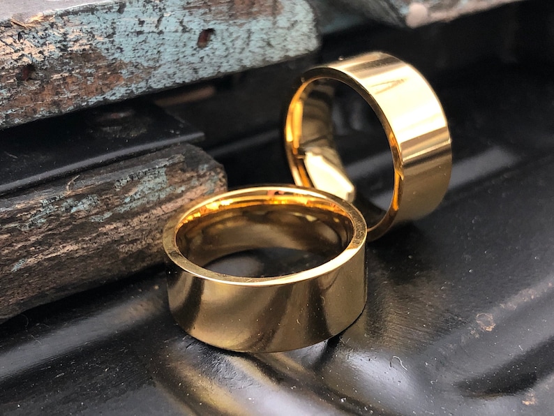 May include: Two gold-colored metal rings, one slightly larger than the other, are stacked on top of each other. The rings are smooth and have a polished finish.