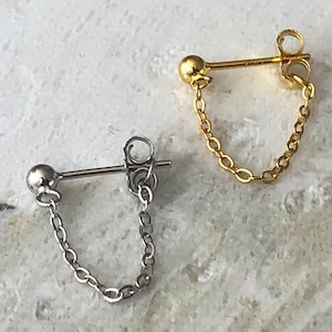 May include: Two pairs of earrings with a small ball and a chain hanging down. One pair is silver and the other is gold.