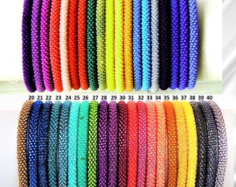 May include: A collection of forty cylindrical beaded bracelets arranged in two rows, numbered 1 through 40. Each bracelet features a uniform texture of small, tightly woven beads in a wide spectrum of solid colours, including purple, red, orange, yellow, green, blue, black, and metallic tones.