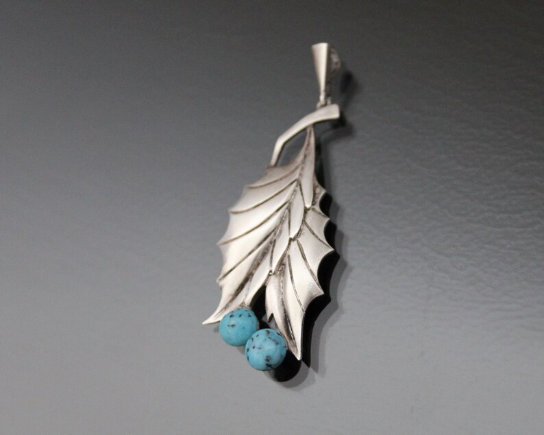 Peut inclure: Un pendentif en argent en forme de feuille avec deux pierres bleu turquoise.