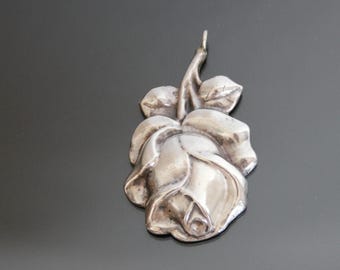 Può includere: Un ciondolo d'argento a forma di rosa. La rosa è dettagliata con petali e foglie.