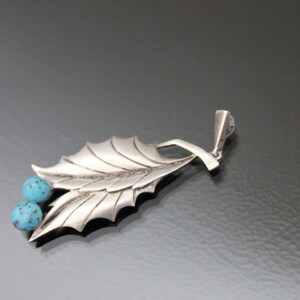 Peut inclure: Un pendentif en argent avec un motif de feuille et deux pierres turquoise.