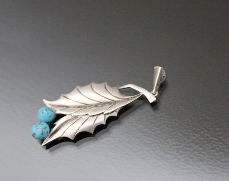 Peut inclure: Un pendentif en argent avec un motif de feuille et deux pierres turquoise.