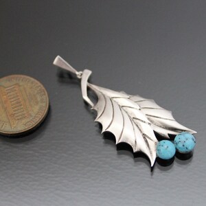 Peut inclure: Un pendentif en argent avec un motif de feuille et deux pierres turquoise. Le pendentif est &agrave; peu pr&egrave;s de la taille d'une pi&egrave;ce de monnaie fran&ccedil;aise.