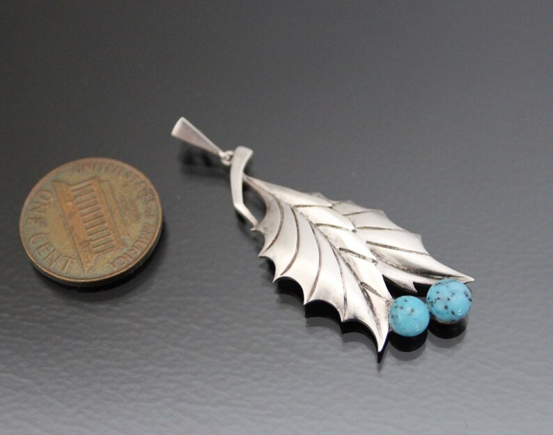 Peut inclure: Un pendentif en argent avec un motif de feuille et deux pierres turquoise. Le pendentif est &agrave; peu pr&egrave;s de la taille d'une pi&egrave;ce de monnaie fran&ccedil;aise.