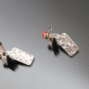 Puede incluir: Un par de gemelos de plata con un dise&ntilde;o rectangular martillado y un acento de piedra roja.