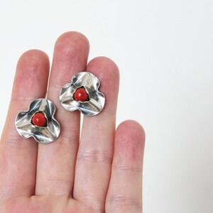 Puede incluir: Un par de pendientes de plata con un centro de coral rojo. Los pendientes tienen forma de flor con tres p&eacute;talos.