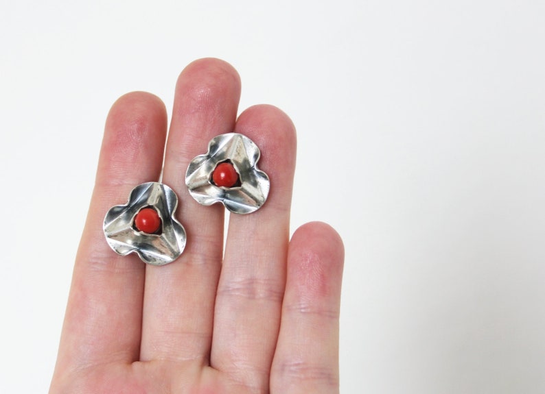 Puede incluir: Un par de pendientes de plata con un centro de coral rojo. Los pendientes tienen forma de flor con tres p&eacute;talos.