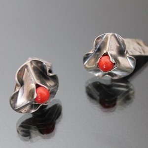Puede incluir: Un par de pendientes de plata con una piedra de coral rojo en el centro de cada pendiente. Los pendientes tienen forma de flor con una superficie texturizada.