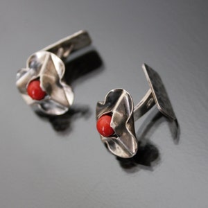 Puede incluir: Un par de gemelos de plata con una piedra de coral rojo en el centro de cada gemelo. Los gemelos tienen forma de flor.