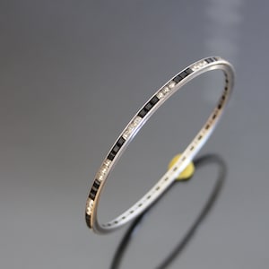 Pode incluir: Um bracelete de prata com uma fila de pedras quadradas pretas e brancas.