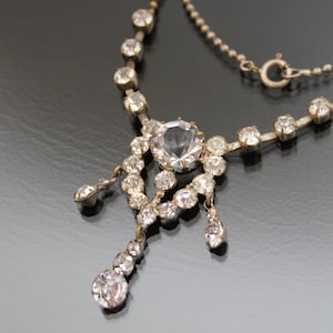 May include: A silver necklace with a large clear rhinestone pendant. The pendant is surrounded by smaller rhinestones and has three dangling strands of rhinestones.
