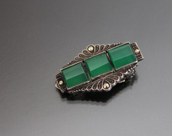 May include: A silver brooch with three square green stones set in a filigree design.