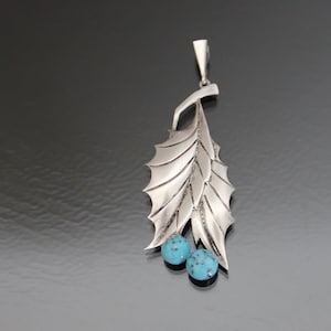 Peut inclure: Un pendentif en argent avec un motif de feuille et deux pierres turquoise.
