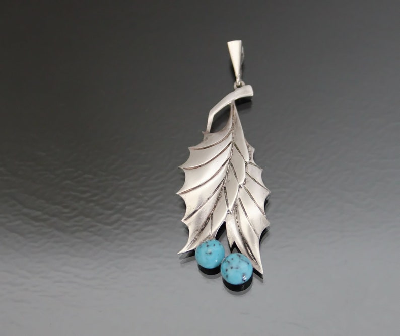 Peut inclure: Un pendentif en argent avec un motif de feuille et deux pierres turquoise.