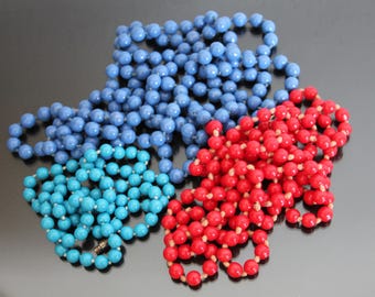 May include: Three strands of colorful beads, one blue, one turquoise, and one red. The beads are all round and smooth.