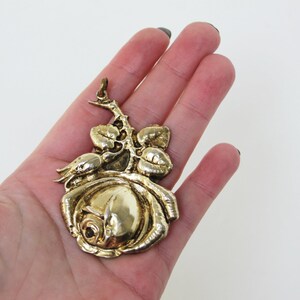 May include: A gold-colored rose pendant with detailed leaves and stem. The pendant is a three-dimensional design, with a loop at the top for hanging. The rose is in full bloom, with intricate petal detailing.