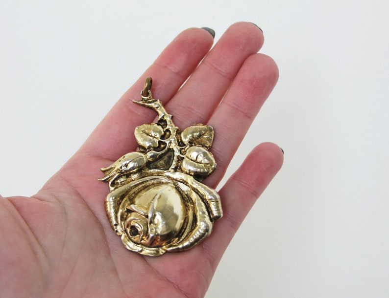May include: A gold-colored rose pendant with detailed leaves and stem. The pendant is a three-dimensional design, with a loop at the top for hanging. The rose is in full bloom, with intricate petal detailing.