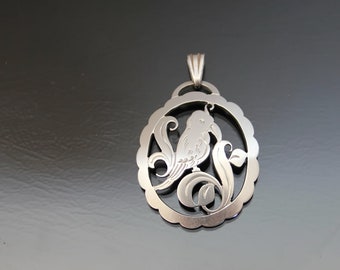 May include: Silver pendant featuring a detailed cutout design of a bird perched on a branch with leaves. The pendant has a smooth, polished finish.