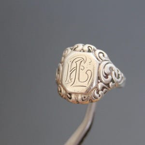 May include: Silver ring with an ornate design and an engraved initial "L" on the face.