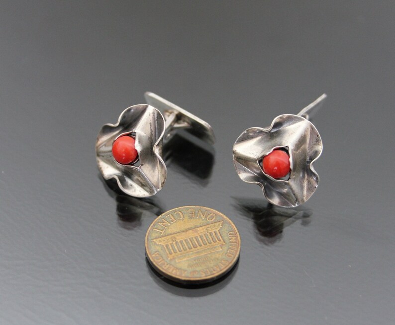 Puede incluir: Un par de gemelos de plata con una piedra de coral rojo en el centro de cada gemelo. Los gemelos tienen forma de flor con cinco p&eacute;talos.