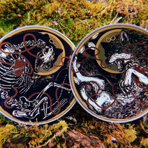 May include: Two round stickers featuring black and white illustrations of a wolf and a skeleton. The wolf is snarling and the skeleton is holding a heart. Both stickers have a gold infinity symbol and red string.