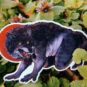 Könnte beinhalten: Ein schwarz-weißer Sticker eines knurrenden Wolfes mit rotem Hintergrund. Der Wolf hat einen blutigen Mund und ist in einer bedrohlichen Pose dargestellt.