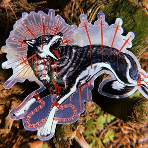 May include: A black and white wolf sticker with red accents. The wolf is depicted with multiple swords piercing its body and a chain around its neck and legs. The sticker has a holographic finish.