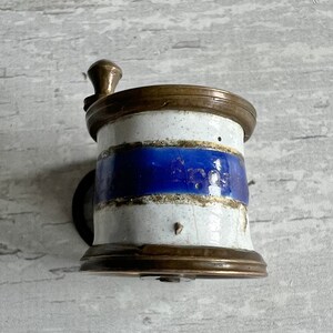 May include: Vintage coffee grinder with a white and blue ceramic body, complemented by brass fittings. The grinder has a hand crank and a cylindrical form, displaying a classic appearance. The blue band provides a striking contrast to the design.
