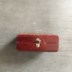 May include: A small, red, wooden box with a gold latch. The box has a textured surface and is closed.