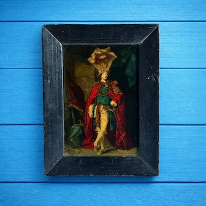 May include: An antique framed painting depicting a figure in regal attire. The figure wears a red cape, green tunic, and a feathered hat. The painting is set against a dark background with a red flag and green drapery. The frame is black.