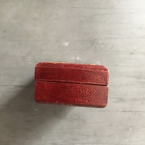 May include: A small, rectangular box with a dark red leather exterior. The box has a hinged lid and a subtle texture.