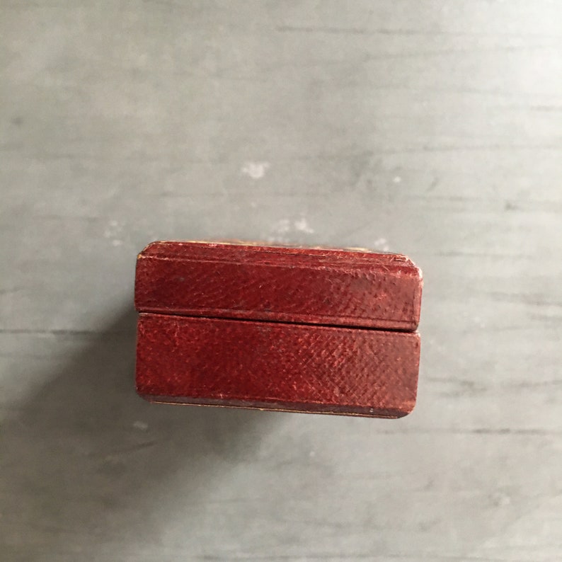 May include: A small, rectangular box with a dark red leather exterior. The box has a hinged lid and a subtle texture.