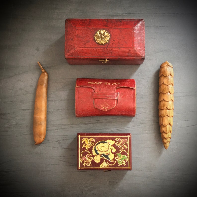 May include: Four vintage boxes with intricate designs. A red box with a gold floral design, a red box with the words "Forget Me Not" in gold lettering, a red box with a gold floral design, and a wooden box with a carved design.