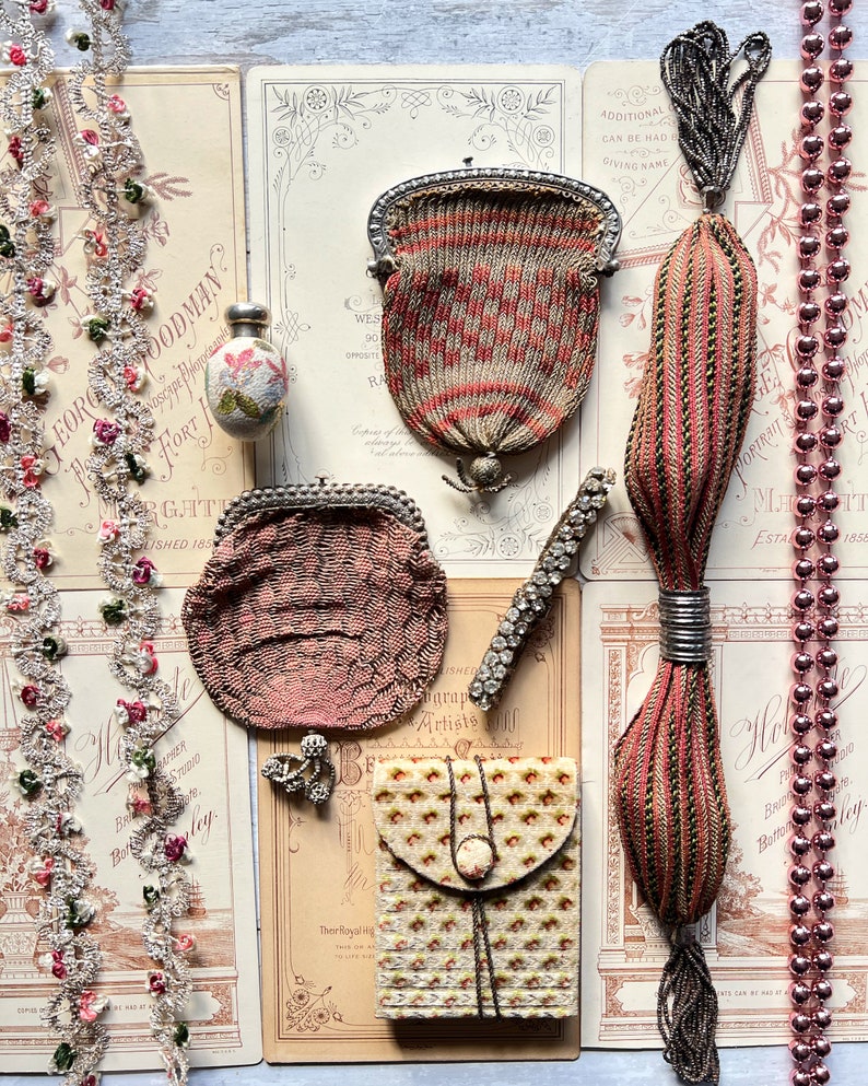 Pode incluir: Uma cole&ccedil;&atilde;o de bolsas e acess&oacute;rios vintage de contas, incluindo uma pequena bolsa de contas rosa, uma bolsa de contas vermelha e branca maior, uma bolsa de contas com borla e uma pequena caixa de contas. Os itens est&atilde;o dispostos em uma mesa com papel e renda antigos.