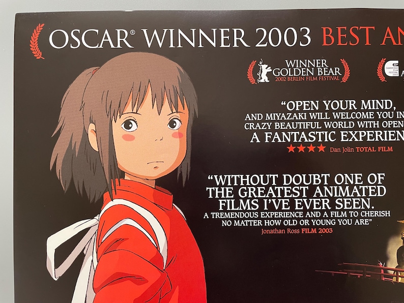 May include: Poster for the animated film, featuring a young girl in a red outfit with white accents. The poster includes text indicating it won an Oscar in 2003 and the Golden Bear award in 2002. Quotes from critics are also featured.