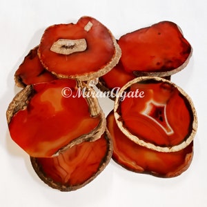 Op de afbeelding: Een set van zes agaat onderzetters in tinten rood en oranje. De onderzetters zijn natuurlijke plakjes agaat met een gepolijste oppervlakte en een ruwe, natuurlijke rand. De agaat heeft een uniek patroon van banden en swirls.