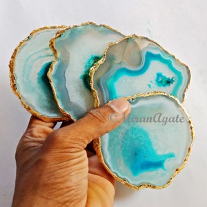 May include: Set of four agate coasters with gold trim. The coasters are a light blue and white color with a swirling pattern. The coasters are perfect for protecting your furniture from scratches and spills.