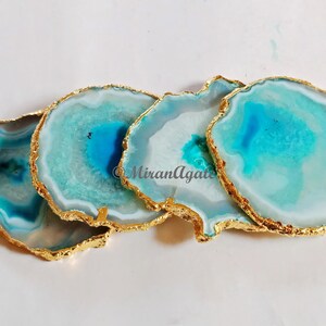 May include: Four agate coasters with gold trim. The coasters are a light blue and white color with a swirling pattern.